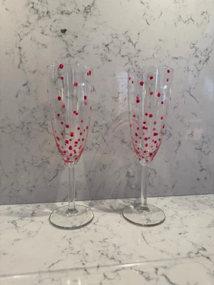 Champagneglas med röda prickar - Två höga champagneglas i genomskinligt glas med handmålade röda och rosa prickar som dekoration. Perfekta för att göra firandet lite extra festligt och unikt. Glasen har klassisk form med smal kupa och lång fot.