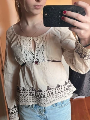 Odd Molly broderad blus - Snygg cremefärgad blus från odd molly. Den är dekorerad med mörkbruna broderier längs nederkant och ärmslut. Blusen har spetsdetaljer och knytning vid halsen samt en broderad fågel på ena ärmen. Tillverkad i ett tunt, luftigt material och har lång ärm. Jag vet inte exakt vad det är för storlek men jag har srl xs och den sitter lite löst så jag rekommenderar den till dig som har runt S eller M