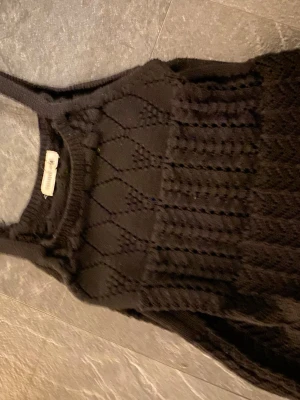 Svart spetstopp  - Snygg svart virkad topp med breda axelband och ett genombrutet mönster i garn. Toppen har en rund halsringning och är perfekt för lager på lager eller till sommaren. Materialet är mjukt och stretchigt för en bekväm passform.