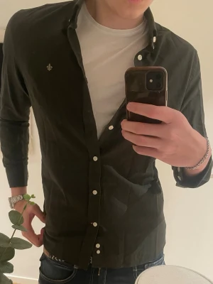 Svart skjorta från Morris Stockholm - Snygg svart skjorta från Morris Stockholm i storlek M. Skjortan har klassisk krage, vita knappar och en liten broderad logga på bröstet. Tillverkad i mjuk bomull och passar perfekt till jeans eller chinos.