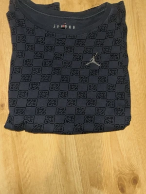  Jordan t-shirt med 23-mönster - Snygg svart t-shirt från Jordan med all-over print av siffran 23 och Jumpman-logga på bröstet. T-shirten har rund hals och är perfekt för dig som gillar sportig streetstyle.