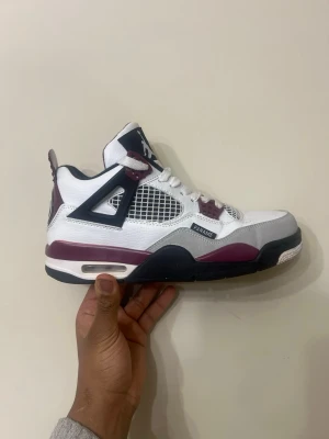 Nike Jordan 4 Bordeaux sneakers - Nike Jordan 4 Bordeaux sneakers med vit ovandel i skinn, detaljer i vinrött och grått, svarta inslag och meshpaneler på sidorna. Klassisk Jumpman-logga på plösen och snörning framtill. Snygg och ikonisk siluett med platt sula och rund tå.PSG edition