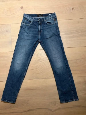 Blå jeans från Replay - Snygga blå jeans från Replay med klassisk femficksmodell och raka ben. Jeansen har en lätt tvättad look med subtila slitningar och detaljerade bakfickor med vågmönster. Tillverkade i bomull för en bekväm känsla och stilren passform.