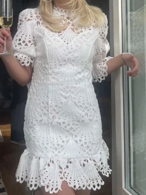 Vit spetsklänning med volang - Superfin vit kortklänning i spets med puffiga trekvartsärmar och volangkant nedtill. Klänningen har ett detaljerat broderat mönster och rund halsringning. Perfekt till student eller sommarens fester.