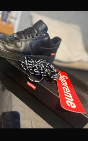 Nike Air Force 1 x Supreme  - Nike Air Force 1 Low Supreme i helsvart skinn med Supreme-logga på sidan och boxen. Klassisk siluett med rund tå, snörning och platt sula. Medföljer extra svarta Supreme-skosnören. Äkta supreme skor!