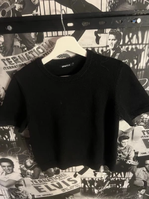 Svart stickad topp från Ginatricot - En svart, stickad topp från Ginatricot med korta ärmar och rund halsringning. Modellen är croppad och har en enkel, stilren design som passar perfekt till jeans eller kjol.