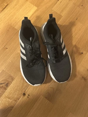 Adidas svarta sneakers med vita ränder - Snygga svarta Adidas sneakers med klassiska vita ränder på sidorna. Fint skick men lite smutsiga undertill. Mjuk o skön sula att gå i 