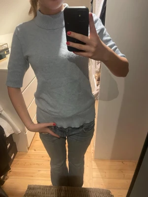 Ljusgrå polotröja med trekvartsärm - Säljer en ljusgrå polotröja med korta ärmar och ribbade muddar. Tröjan har en mjuk och stretchig känsla, perfekt för lager på lager. Enkel och stilren design som passar till det mesta.