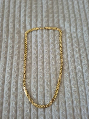 Stainless steel guld halsband - Snyggt guld halsband med en unik, detaljerad kedjedesign. Länkarna har ett coolt mönster som ger halsbandet en modern och trendig look. Perfekt för att lyfta vilken outfit som helst med lite extra bling.