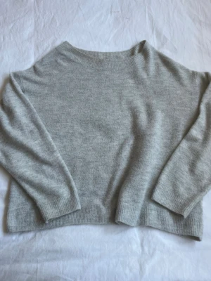 Ljusgrå oversize stickad tröja - Mysig ljusgrå stickad tröja i oversize-modell med rund halsringning och långa ärmar. Tröjan har ribbade muddar vid ärmslut och nederkant, perfekt för lager-på-lager-stil. Enkel och stilren design som passar till det mesta.