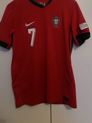 Portugal fotbollströja Nike Ronaldo 7 - Först och främst så köptes denna för 1200 så priset är igenkligen väldigt bra. 👍 Säljer en röd Portugal fotbollströja från Nike med nummer 7 och Ronaldo på ryggen. Tröjan har svarta detaljer vid ärmslut och krage samt landslagets emblem på bröstet. Perfekt för dig som älskar fotboll och vill stötta Portugal.