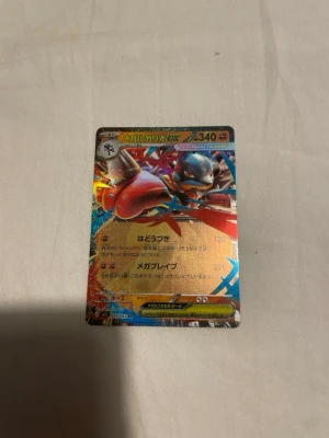Pokémonkort Mega Lucario EX japansk - Säljer ett japanskt Pokémonkort med Mega Lucario EX-motiv. Kortet har en holografisk yta med färger i rött, blått och silver. Texten är på japanska och kortet har 340 HP. Perfekt för samlare eller Pokémonfans.