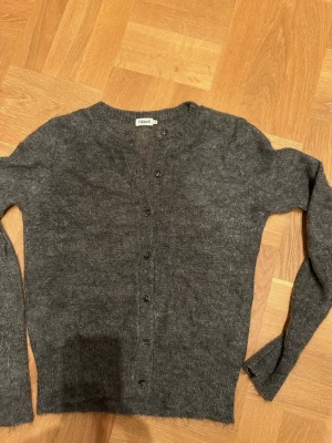 Mjuk och skön kofta Filippa K - Stilren mörkgrå kofta från Filippa K med rund halsringning och knäppning framtill. Långärmad modell i mjukt mohair, perfekt att slänga över en t-shirt eller blus. Enkel och tidlös design som passar till det mesta.