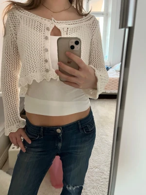 Vit virkad kofta - Säljer en söt vit virkad cropped kofta med långa ärmar. Koftan har vågig kant nertill och vid ärmslut. Perfekt att styla över ett linne eller topp🥰