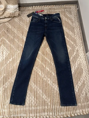 Replay jeans helt nya - Snygga mörkblå jeans från replay. Jeansen har en snygg slim passform och är tillverkade i mjuk bomull med lite stretch för extra komfort. Perfekta till alla dina outfits och har en tidlös look. Helt oanvända med lappar osv kvar storlek 14A 158 cm. Hör av er vid eventuella frågor! 