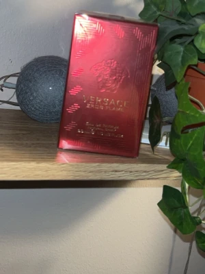 Versace Eros Flame Eau de Parfum - Versace Eros Flame Eau de Parfum i en snygg röd och guldig kartong. Parfymen har en lyxig känsla och är perfekt för dig som gillar exklusiva dofter. Förpackningen är rektangulär och tillverkad av kartong med glansig finish.