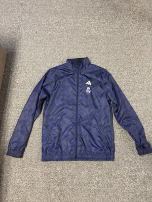 Adidas Real Madrid vindjacka blå - Säljer en addidas dubbel vindjacka en sida är lila och en svart gul man byter på de hur man vill använd endast 3-4 gånger jätte snygg att ha på sig storlek S
