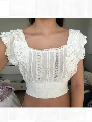 Vit broderad croppad blus - Supersöt vit croppad blus med broderade detaljer och spetsinslag. Toppen har smockad midja som ger en snygg passform. Perfekt till jeans eller kjol i sommar💗 Köpt i Spanien på ”Pimkie”. Storlek S men passar även xs.