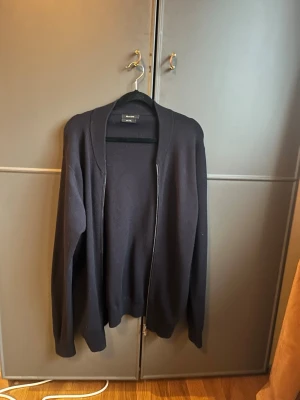 Mörkblå ziptröja från Oscar Jacobson - Klassisk mörkblå ziptröja från Oscar Jacobson. Tröjan har en rak passform, ribbade muddar och dragkedja framtill. Tillverkad i mjukt material som känns skönt mot huden. Perfekt för lager på lager och enkel att matcha med olika outfits.