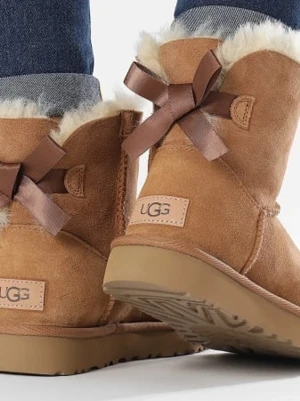 UGG boots - Säljer ett par klassiska bruna UGG boots i mocka med fluffig vit insida och söta bruna rosetter bak. Skorna har en låg skaftmodell och grov sula som ger bra grepp. Perfekta för kalla dagar när du vill vara både varm och stylish.Helt nya i kartong!Butikspris 2.100:-