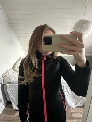 Svart vindjacka med rosa dragkedja - Snygg svart vindjacka med rosa dragkedjor och detaljer. Jackan har hög krage och figurnära passform, perfekt för blåsiga dagar. Praktiska fickor med dragkedja och sportig look. Sitter som en s!