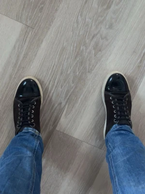 Lanvin - Snygga mörkbruna lanvin med vit sula och svarta skosnören. Ovandelen är i läder med blanka svarta tår och mattsvarta sidor. Klassisk låg modell med metallöljetter och stilren design som passar till jeans och streetwear.