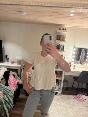 Vit volangblus med kort ärm - Söt vit blus med volang nertill och korta ärmar. Modellen är luftig och har en avslappnad passform, perfekt till jeans eller kjol. Enkel och stilren design som passar till många tillfällen.