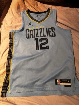 Memphis Grizzlies basketlinne Morant - Ljusblått Memphis Grizzlies basketlinne med nummer 12 och namnet Morant på ryggen. Linnet har svarta och gula detaljer, meshmaterial för andningsförmåga och Dri-FIT-teknologi. Snygg design med klubbnamn och logga framtill. Priset kan diskuteras 