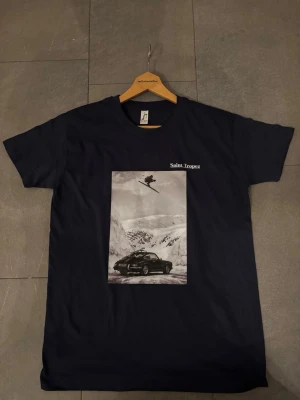 Svart Saint Tropez t-shirt med tryck - Svart t-shirt med tryck av  Saint Tropez med ett stort svartvitt tryck på bröstet som visar en bil i snölandskap och en skidåkare i luften. T-shirten har rund hals och korta ärmar. Perfekt för dig som gillar streetwear och unika motiv. Tröjan finns i storlek S, M, L  