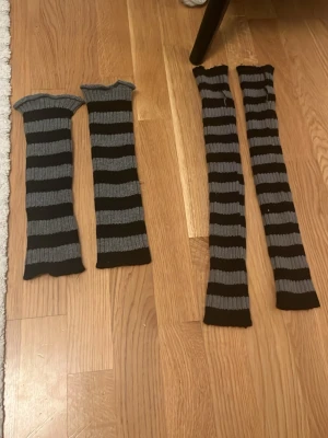 Randiga benvärmare i svart och grå - Två par ribbade benvärmare i svart och grått med breda horisontella ränder. Stickad design som ger en mjuk och stretchig känsla, perfekta för att addera en alternativ vibe till din outfit. Passar både till kjol och byxor.