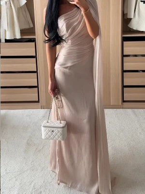 Festklänning Jluxlabel  - Elegant långklänning i ljus champagnefärg med oneshoulder-design och draperad överdel. Klänningen har en hög slits och ett svepande tyg som ger en exklusiv känsla.. Använd i några timmar bara.