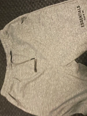 Grå Essentials mjukisbyxor - Säljer ett par grå mjukisbyxor från Essentials med dragsko i midjan och fickor på sidorna. Byxorna har en relaxed fit och logga tryckt på benet. Perfekta för chill dagar eller när du vill ha det extra bekvämt.