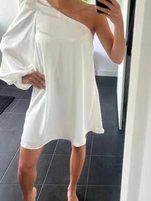 Vit oneshoulder kortklänning - En vit kortklänning i oneshoulder-modell med en lång puffärm. Klänningen är från NAKD och aldrig använd, lappen sitter kvar💕