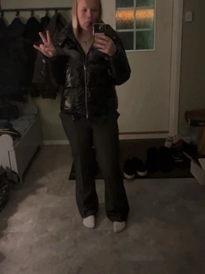 Mörkgrå kostymbyxor med pinstripes - Snygga mörkgrå kostymbyxor med diskreta vita pinstripes och klassisk bootcut-form. Byxorna har fickor fram och är tillverkade i ett mjukt och följsamt material som ger en stilren look. Perfekta för dig som vill ha en dressad och trendig stil. Fejkficka på baksidan av byxorna på högersidan. 