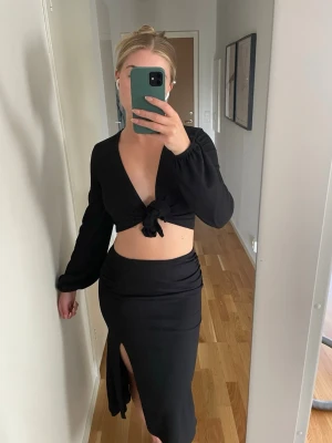 Svart set med knyt och slits  - Säljer ett svart tvådelat set med långärmad topp som knyts framtill och en matchande kjol med hög slits. Från Gina tricot, använd 1 gång, köptes förra sommaren. 