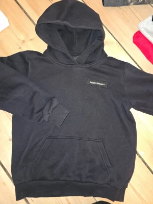 Svart hoodie från Peak Performance - Snygg svart hoodie från Peak Performance med klassisk logga på bröstet. Hoodien har en stor känguruficka framtill, ribbade muddar vid ärmar och nederkant samt en rejäl huva. Perfekt för en avslappnad och sportig stil. 