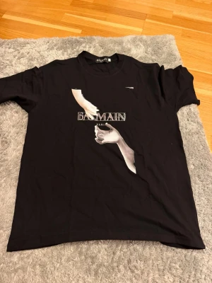 Svart Balmain Paris t-shirt - Snygg svart t-shirt från Balmain Paris med tryck av två händer och logga på bröstet. Klassisk rund hals och korta ärmar. Tillverkad i mjuk bomull för en bekväm känsla och stilren look.