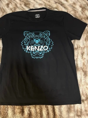 Svart Kenzo t-shirt med tigertryck - Snygg svart t-shirt från Kenzo med det ikoniska tigertrycket i turkos och vitt på bröstet. Klassisk rund hals och korta ärmar. Tillverkad i mjuk bomull för en bekväm känsla och stilren look.