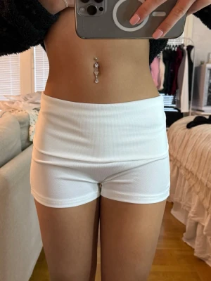 Vita låga shorts i ribbad!  - Säljer ett par vita, högmidjade shorts i ribbad bomull. De har en tight passform och är perfekta för sommarens varma dagar. Stilrena och enkla att matcha med olika toppar. Supersköna och trendiga shorts för dig som gillar en clean look.