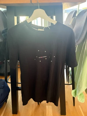 Svart Saint Laurent t-shirt helt ny med tagg - Helt ny med tagg, Snygg svart t-shirt från Saint Laurent med små vita stjärnor och logga på bröstet. Klassisk passform och rund halsringning. Perfekt till jeans eller shorts för en clean look.