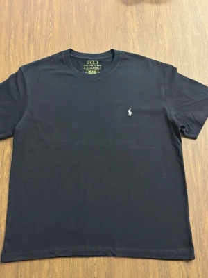 Svart t-shirt från Polo Ralph Lauren - Klassisk svart t-shirt från Polo Ralph Lauren med rund halsringning och den ikoniska vita logobrodyr på bröstet. Start priset 500 kr. 