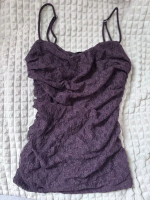 Spetstopp från Bikbok - Plommonfärgad spetstopp från Bikbok i storlek xs. Funkar väldigt bra som festtopp! Axelbanden är justerbara och toppen har en liten draperad eller "hängig" look vid byst men är ganska åtsittande i midjan! Toppen är oanvänd, säljer eftersom jag inte tycker jag passar i denna färg.
