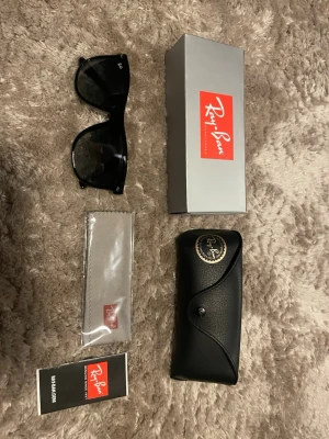 Svarta Ray-Ban solglasögon - Klassiska svarta solglasögon från Ray-Ban med bred båge och mörka glas. Snygg och fräsch design som passar till det mesta. Kommer med originalfodral, putsduk och box. Bara att höra av dig om du har någon fråga!