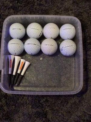 Golfbollar Titleist Pro V1 + peggar - Säljer ett set med åtta vita Titleist Pro V1 golfbollar och fyra vita peggar med svart fot och orange text. Perfekt för dig som vill fylla på golfutrustningen med kvalitetsbollar och peggar. Bollarna är i ok skick. Kontakta vid frågor! 
