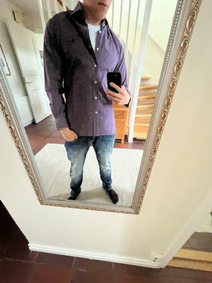 Rutig skjorta från Polo Ralph Lauren - Snygg rutig skjorta från Polo Ralph Lauren i mörklila och vit. Klassisk modell med knappar framtill och lång ärm. Tillverkad i mjuk bomull som känns skön mot huden. Perfekt för dig som vill ha en stilren och tidlös look.