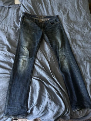 Slim fit jeans från American Eagle - Snygga blå slim fit jeans från American Eagle med klassisk femficksdesign och slitna detaljer. Tillverkade i 100% bomull för en autentisk denimkänsla. Perfekta för dig som gillar en smalare passform och vill ha ett par jeans som funkar till det mesta.