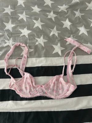 Ljusrosa blommig bikini top - Söt ljusrosa bikini överdel  med små blommor i blått och rosa. , justerbara axelband och spetsdetaljer längs kanterna. Perfekt för dig som gillar romantisk och feminin stil. Aldrig använd 