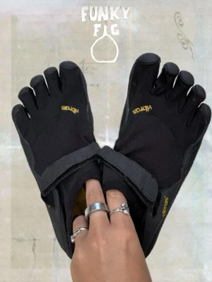 Barfota skor - Vibram FiveFingers  - Svarta Vibram FiveFingers med separata tår och kardborreband över foten. Skorna är tillverkade i mesh och syntetmaterial för bra andningsförmåga och flexibilitet. Perfekta för dig som gillar barfotakänsla och vill att fötterna ska må bra! 