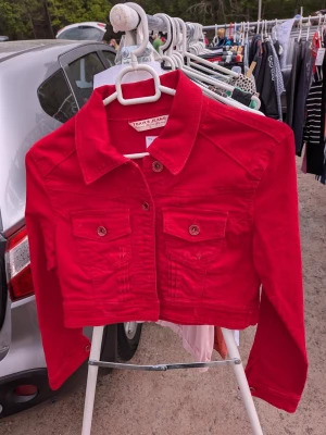 Röd jeansjacka - Snygg röd jeansjacka med klassisk krage, två bröstfickor med knappar och knappstängning framtill. Jackan har långa ärmar och en croppad passform som ger en trendig look. Perfekt att styla till dina favoritjeans eller kjol.