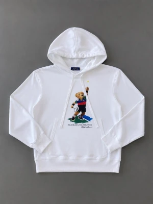 Vit hoodie Polo Bear Ralph Lauren - Vit hoodie från Polo Ralph Lauren med den ikoniska Polo Bear-trycket framtill. Klassisk känguruficka och dragsko i huvan. Tillverkad i mjuk bomull för skön känsla. Perfekt för en avslappnad och stilren look.